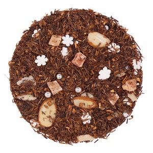 May include: A close-up of a blend of loose leaf tea with dried fruit pieces, white sugar flowers, and silver beads. The tea is a dark brown color and the fruit pieces are a light brown color.