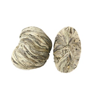 May include: Two dried tea buds, one shaped like a heart and the other round, are made of tightly woven green and white tea leaves.