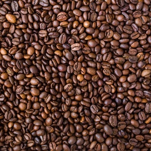 May include: A close-up image of a large quantity of roasted coffee beans. The beans are dark brown and have a slightly oily sheen.