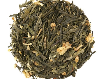 May include: A close-up of a pile of loose leaf green tea with dried jasmine flowers. The tea is a blend of green tea leaves and white jasmine blossoms.