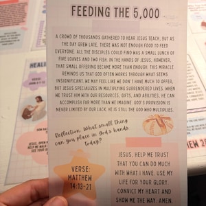 Może przedstawiać: Prostokątna karta dewocyjna zatytułowana Feeding the 5,000 z tłem w kratkę. Zawiera czarny tekst opisujący biblijny cud, małą ilustrację chleba, brzoskwiniową gwiazdę z napisem Matthew 14:13-21 oraz modlitwę.