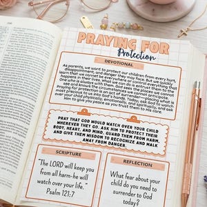 May include: An open book featuring a devotional page titled PRAYING FOR PROTECTION with sections for Scripture and Reflection. The page includes a grid background, orange borders, and text about child safety. A rose gold pen rests on the right side.