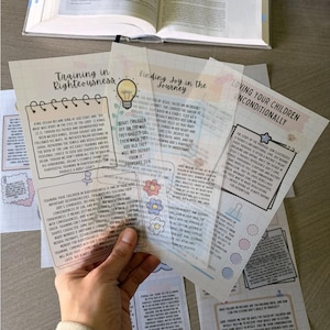 May include: A hand holds several translucent sheets with text and illustrations. The sheets have titles like "Training in Righteousness" and "Finding Joy in the Journey." An open book is visible in the background.
