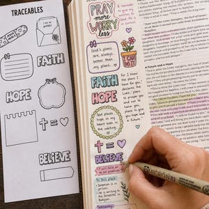 May include: A journal page with colourful handwritten notes and illustrations. The page includes the words "Faith," "Hope," and "Believe," along with Bible verses and decorative elements. A hand is writing with a black pen.