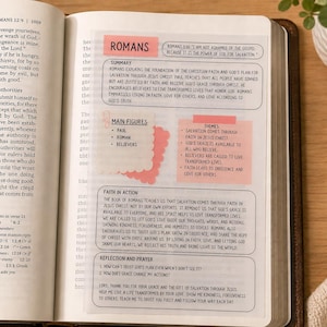May include: Open Bible with a page marked with pink sticky notes. The notes contain text about the book of Romans, including summaries, main figures, themes, and faith in action. A pen rests on the wooden surface.