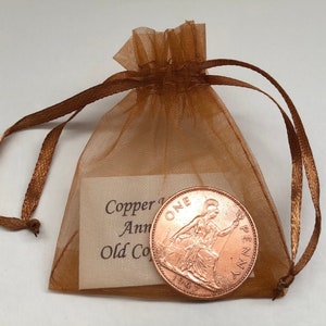 May include: A copper one penny coin from 1967 in a brown organza bag with a tag that reads "Copper 1st Anniversary Old Coin".
