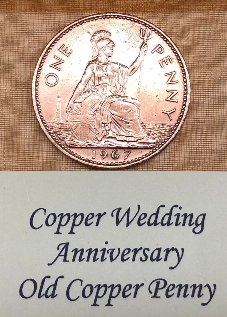 May include: A copper penny coin from 1967 with the inscription "ONE PENNY" and a depiction of Britannia. The coin is on a light brown surface with the text "Copper Wedding Anniversary Old Copper Penny".