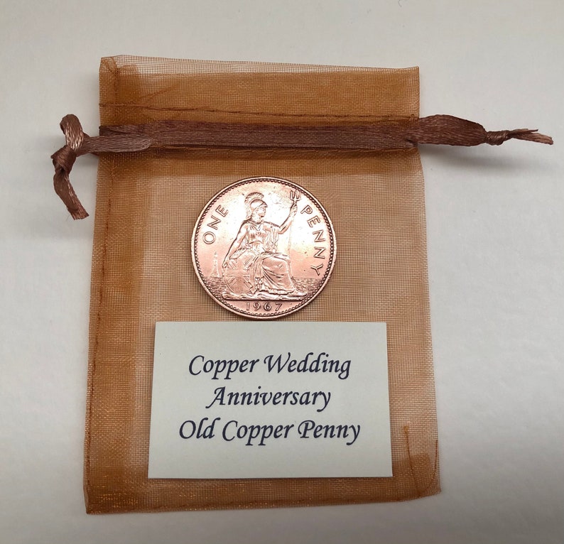 May include: A brown mesh bag with a copper-colored 1967 British One Penny coin inside. The bag has a white tag that reads "Copper Wedding Anniversary Old Copper Penny".
