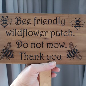 May include: Wooden sign with a bee-friendly wildflower patch message. The sign reads "Bee friendly wildflower patch. Do not mow. Thank you." and features four black and yellow bee illustrations.