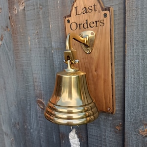 May include: A brass bell with a white rope attached to it. The bell is mounted on a wooden plaque with the words "Last Orders" engraved on it.