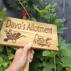 May include: A wooden sign with the text "Davo's Allotment" engraved on it. The sign features a wheelbarrow with gardening tools and a bunch of carrots and onions.