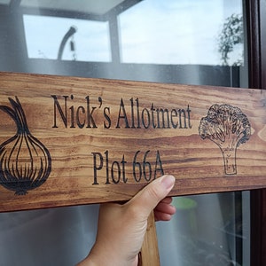 May include: A wooden sign with the text "Nick's Allotment Plot 66A" burnt into the surface. The sign is decorated with an onion and a broccoli illustration.