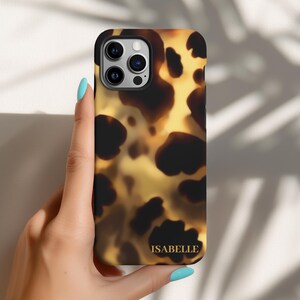 May include: A brown and black iPhone case with a tortoiseshell pattern. The case has a gold inscription that reads "ISABELLE".