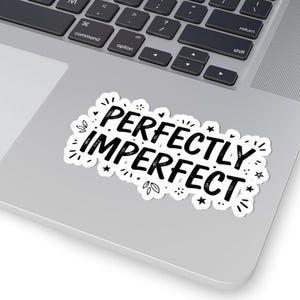 May include: A white sticker with the words "PERFECTLY IMPERFECT" in black, surrounded by small stars and leaves. The sticker is placed on a silver laptop.