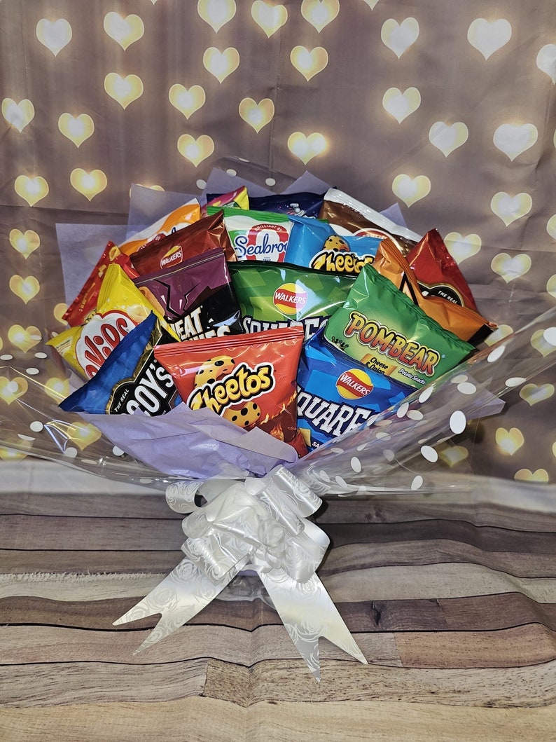 May include: A bouquet of various popular brands of potato chips, including Cheetos, Walkers, and Pombear, wrapped in clear cellophane with white polka dots and a white satin bow.