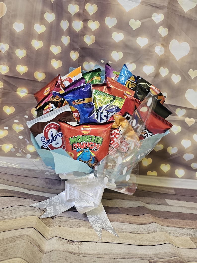 May include: A bouquet of various snack chips and crisps, including Seabrook, Monster Munch, and Cheetos, arranged in a clear plastic wrap with a white ribbon.