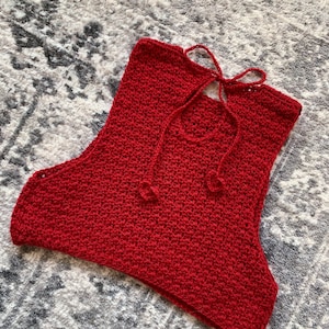 May include: A red crocheted crop top with a tie at the back of the neck.