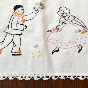 May include: Embroidered linen textile featuring a whimsical design of two figures. One figure, in a clown-like outfit, offers a bouquet to a dancing figure in a dotted dress. The design is outlined in black thread with colorful floral accents.
