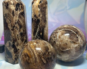 May include: Three polished brown and black banded agate stones. Two are tall, pointed towers and one is a sphere.