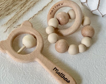 May include: Two wooden baby teethers, one with a handle and a bead that rattles, and the other a ring with beads. Both are engraved with the name "Matthew".