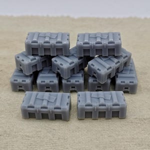 Puede incluir: Una pila de 12 cajas de plástico grises con una superficie texturizada y un diseño en relieve en la parte superior. Las cajas están apiladas en forma de pirámide.