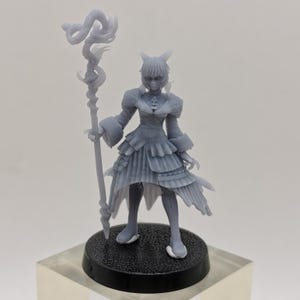 Può includere: Una statuetta in 3D stampata in grigio di un personaggio femminile con orecchie da gatto, che indossa un lungo vestito e tiene un bastone con un design a forma di serpente.