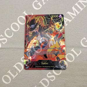 Könnte beinhalten: Rote Sammelkarte mit Sabo aus Dressrosa/Revolutionary Army. Die Karte hat eine Stärke von 5000 und Text zu Spieleffekten. Das Artwork zeigt Sabo mit Flammen und einem Hut.
