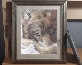 May include: A framed print of a wolf's head with a detailed, realistic style. The wolf is depicted with a brown and gray coat, and its eyes are piercing green. The print is framed in a silver frame with a white mat.