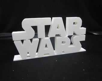 Pode incluir: Um sinal branco impresso em 3D com as palavras "STAR WARS" em uma fonte em negrito e em blocos.