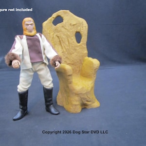 May include: A figure in a white and brown outfit with black boots stands next to a yellow throne-like chair. The figure has a furry collar and a monkey-like face. The text "Action Figure not included" is at the top. Copyright 2026 Dog Star DVD LLC is at the bottom.