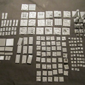 May include: A large collection of gray plastic building blocks, some with intricate designs, for creating miniature models. The blocks are arranged in rows and columns on a gray surface.