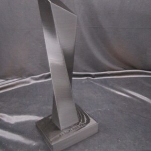 May include: A black, geometric, abstract sculpture with a sharp, angular design. The sculpture is made of a smooth, glossy material and has a tall, slender form.