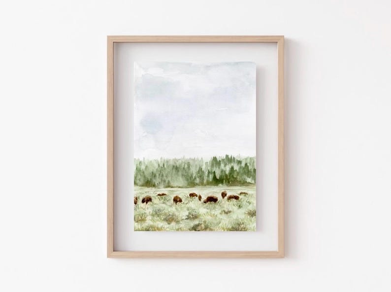 May include: Watercolor painting of a herd of bison grazing in a field with a forest in the background. The sky is a light blue with white clouds.