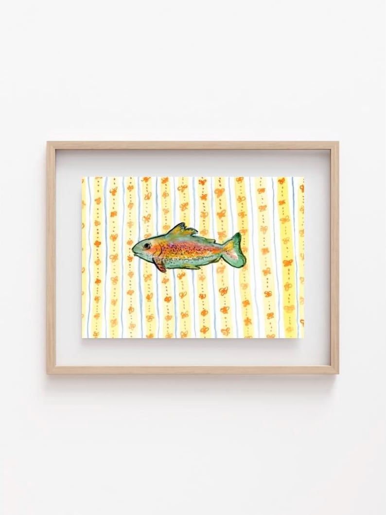 May include: A framed watercolor print featuring a colorful fish with orange, yellow, and green hues. The fish is set against a background of yellow and white vertical stripes adorned with orange butterfly motifs. The frame is a light wood color.