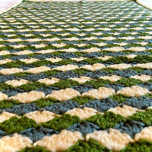 Op de afbeelding: Een gehaakt deken met een chevron-patroon in tinten groen, blauw en wit.