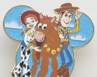 May include: A Disney pin featuring characters from Toy Story. Jessie, Bullseye, and Woody are depicted against a blue sky background with white clouds. The pin has a gold border and is shaped like Mickey Mouse ears.