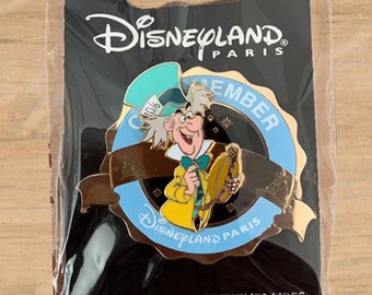 May include: A Disneyland Paris pin featuring the Mad Hatter from Alice in Wonderland. The pin is in a clear plastic package and has a blue and gold design with the words "MEMBER" and "Disneyland Paris".