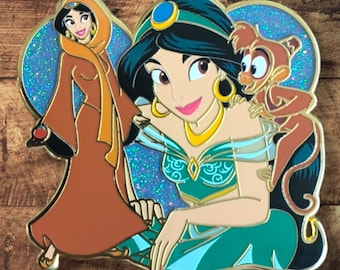 May include: Enamel pin featuring Princess Jasmine in two different outfits, with Abu the monkey. The pin has a glittery blue background and gold accents. Jasmine is wearing a teal and gold outfit and a brown outfit.