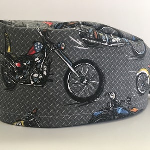 May include: Gray surgical scrub cap with a repeating motorcycle pattern. The cap features illustrations of motorcycles in various colors, set against a diamond plate background. The cap has a tie in the back.