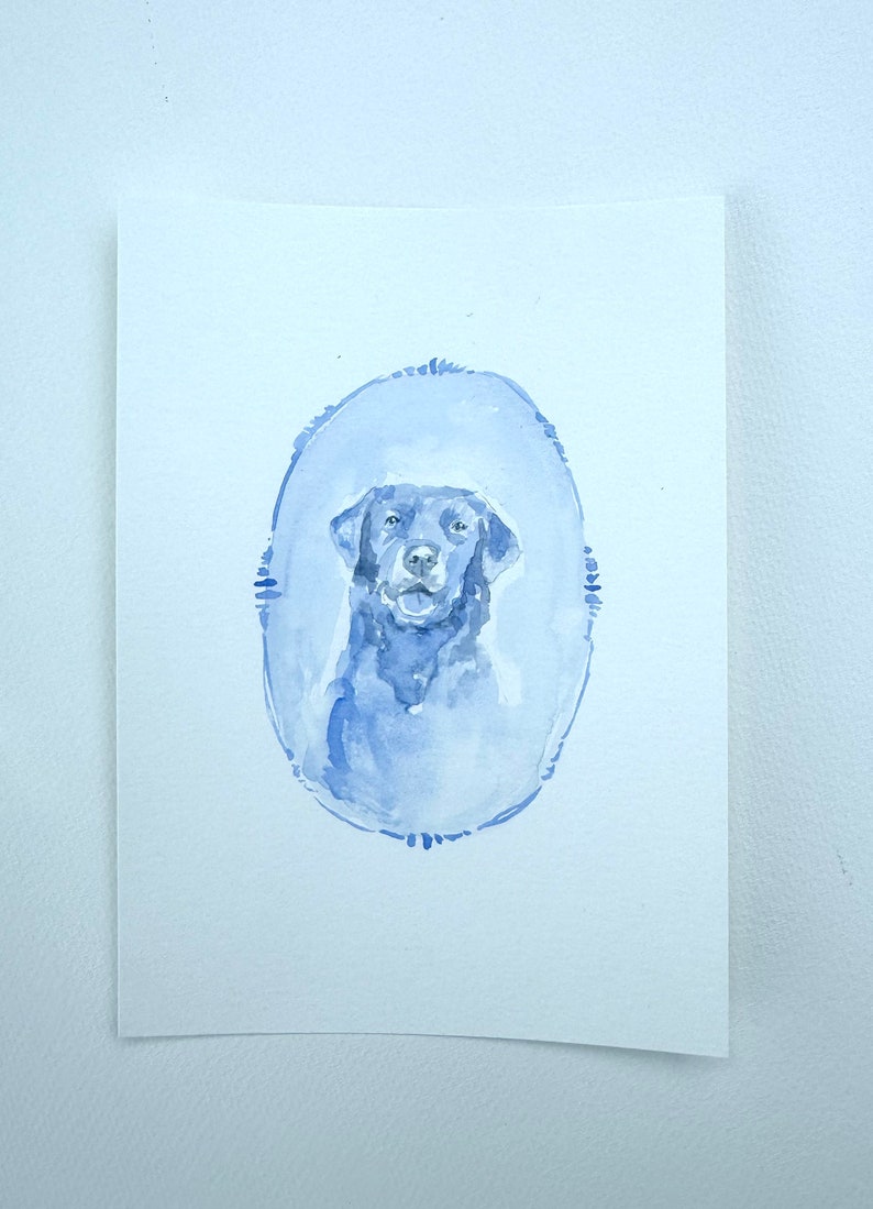 May include: Watercolor painting of a black Labrador Retriever in a blue oval frame.