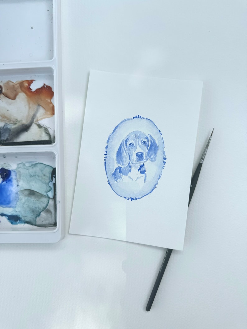 May include: A watercolor painting of a beagle dog in a blue oval frame. The dog is looking directly at the viewer with its ears perked up.
