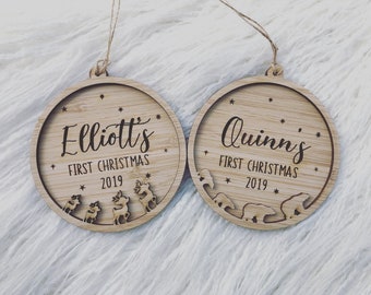 May include: Two round wooden ornaments with a rustic finish. The ornaments are decorated with the text "Elliott's First Christmas 2019" and "Quinn's First Christmas 2019" and feature small reindeer and polar bear cutouts.