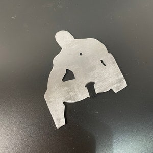 May include: A silver metal cutout of a person in a sitting position. The cutout is a silhouette of a person with arms and legs.