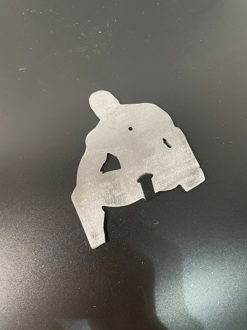 May include: A silver metal cutout of a person in a sitting position. The cutout is a silhouette of a person with arms and legs.