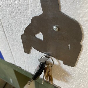 May include: A metal silhouette of a person sitting down with a key ring attached to the bottom. The key ring is holding a set of keys.