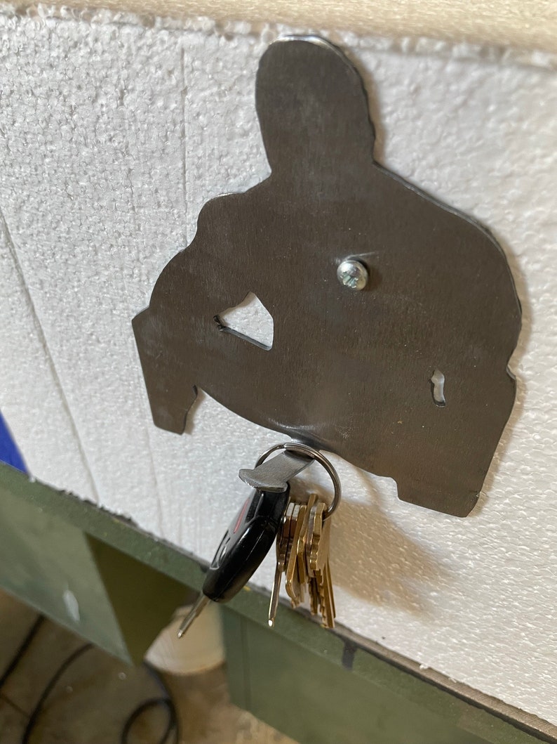 May include: A metal silhouette of a person sitting down with a key ring attached to the bottom. The key ring is holding a set of keys.