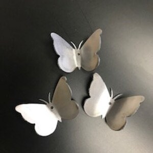 Könnte beinhalten: Drei silberne Metall-Schmetterlingsformen, jede mit einem Loch in der Mitte.