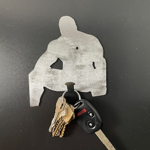 May include: A metal silhouette of a person sitting, with a key ring and keys hanging from the bottom. The keys include a car key with a black fob and the word "PANIC" printed in red.