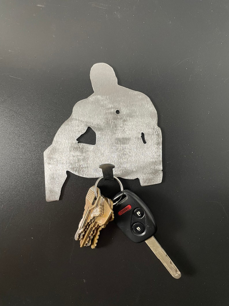 May include: A metal silhouette of a person sitting, with a key ring and keys hanging from the bottom. The keys include a car key with a black fob and the word "PANIC" printed in red.