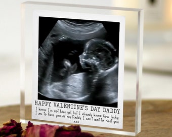May include: A clear acrylic photo frame with a black and white ultrasound image of a baby. The frame has a white background with the text "HAPPY VALENTINE'S DAY DADDY I know I'm not here yet, but I already know how lucky I am to have you as my Daddy I can't wait to meet you XXX".